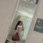 EL Jenny berdiri bergaya di lorong dengan outfit sporty, crop top dan celana pendek hitam.